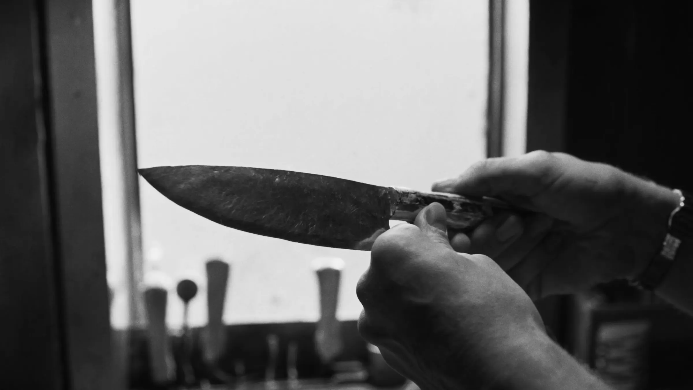 A craftsman checking the edge of a finished knife against the window light