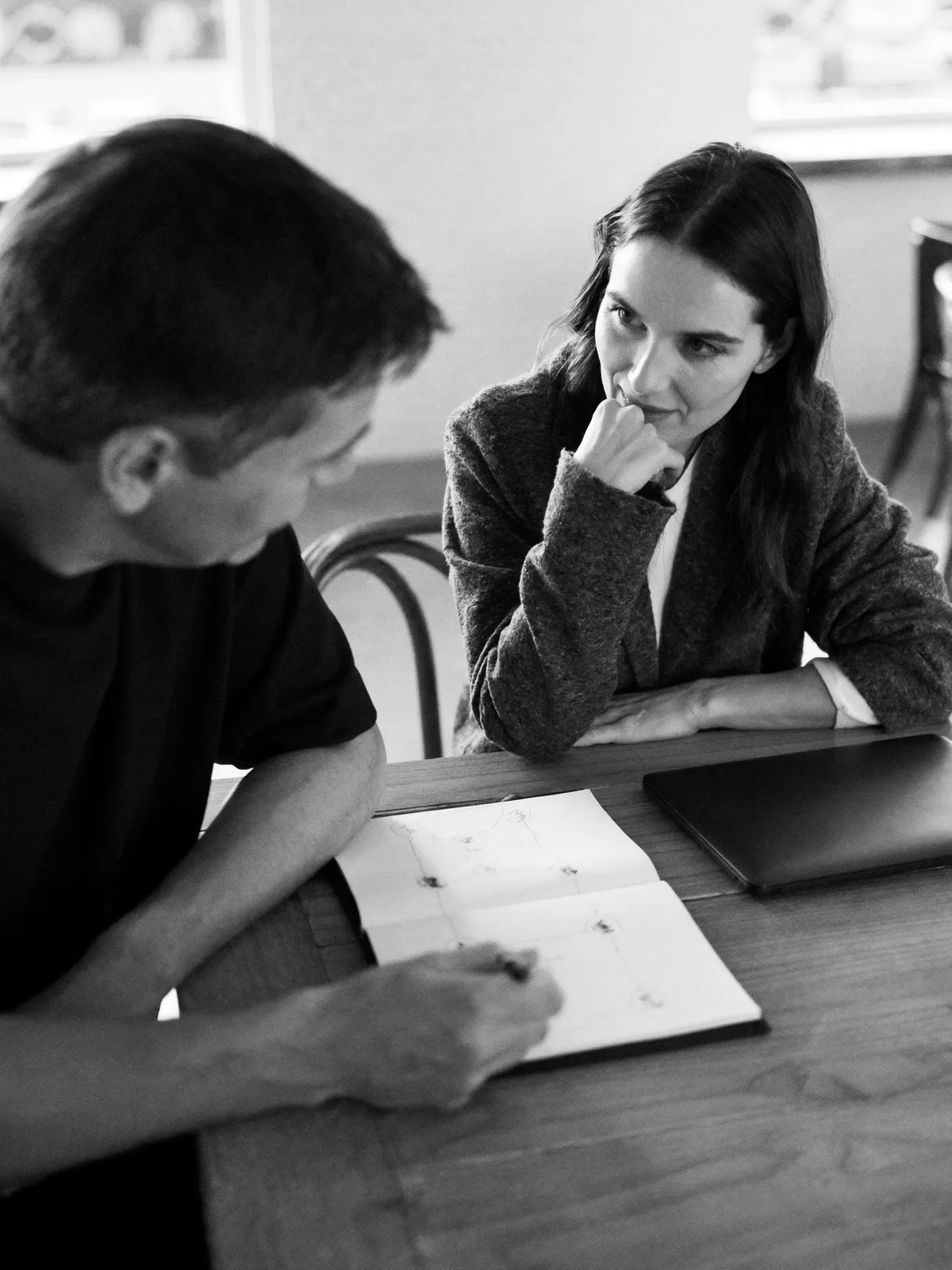 Two people sketching a plan in a notebook at a cafe table