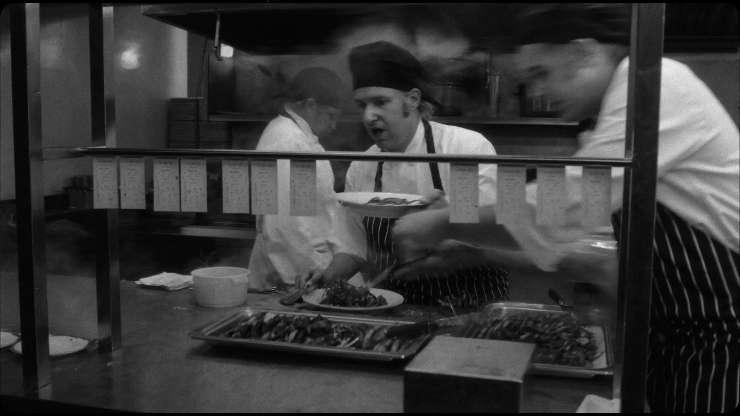An independent restaurant kitchen in full service, chefs plating at the pass